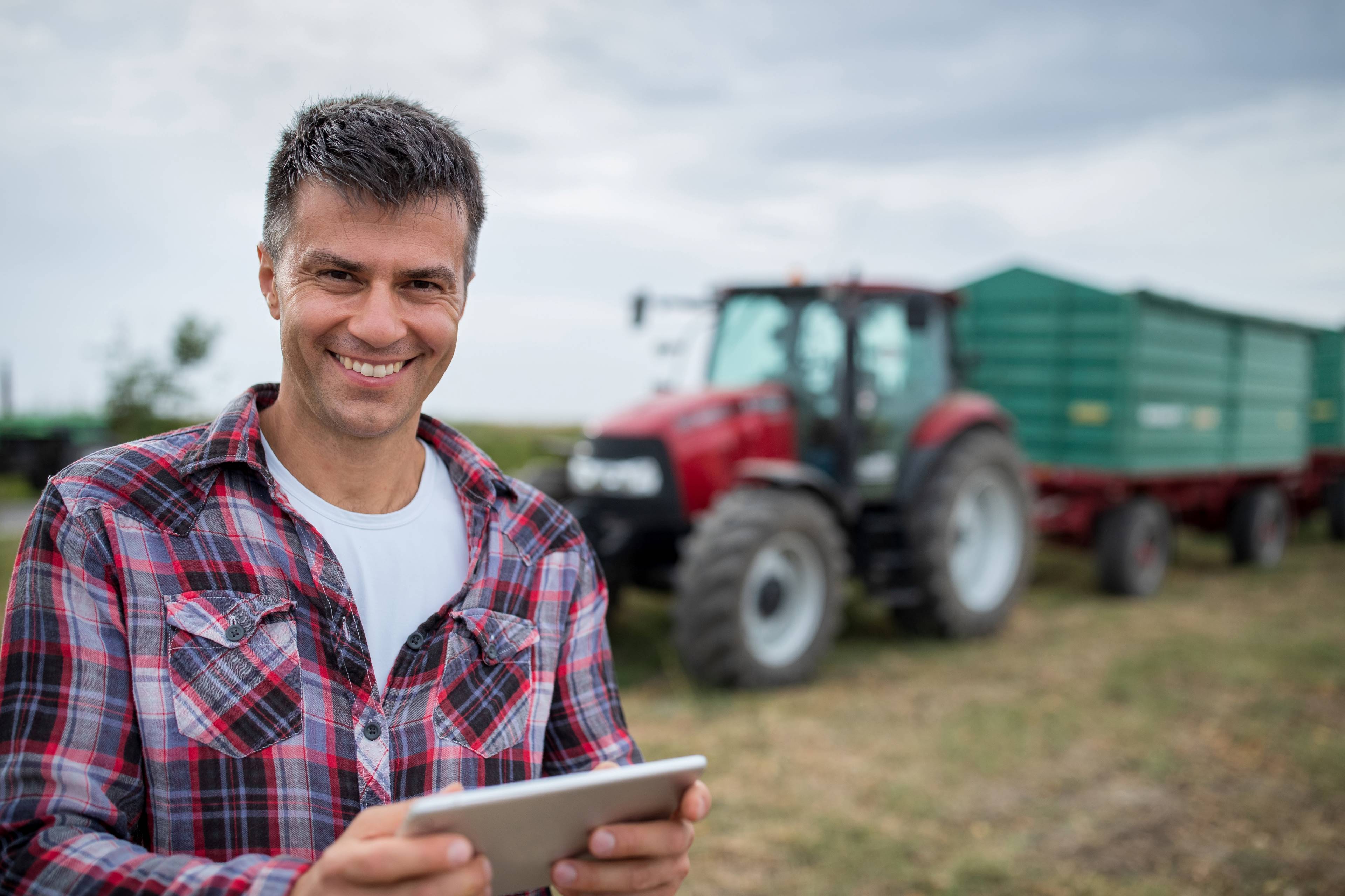 Image of a producer standing in front of a tractor with a tablet