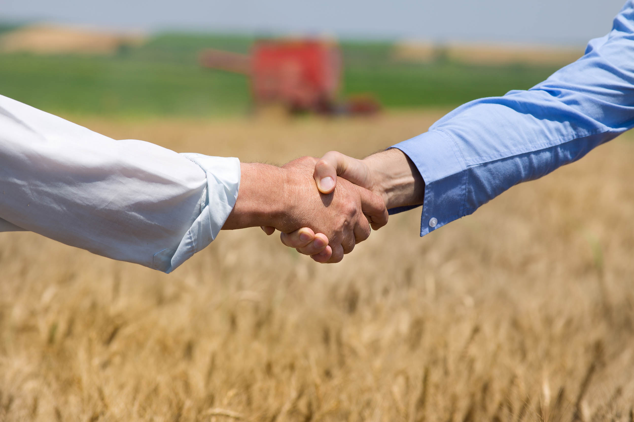 Image of two stakeholders shaking hands in a field of crops
