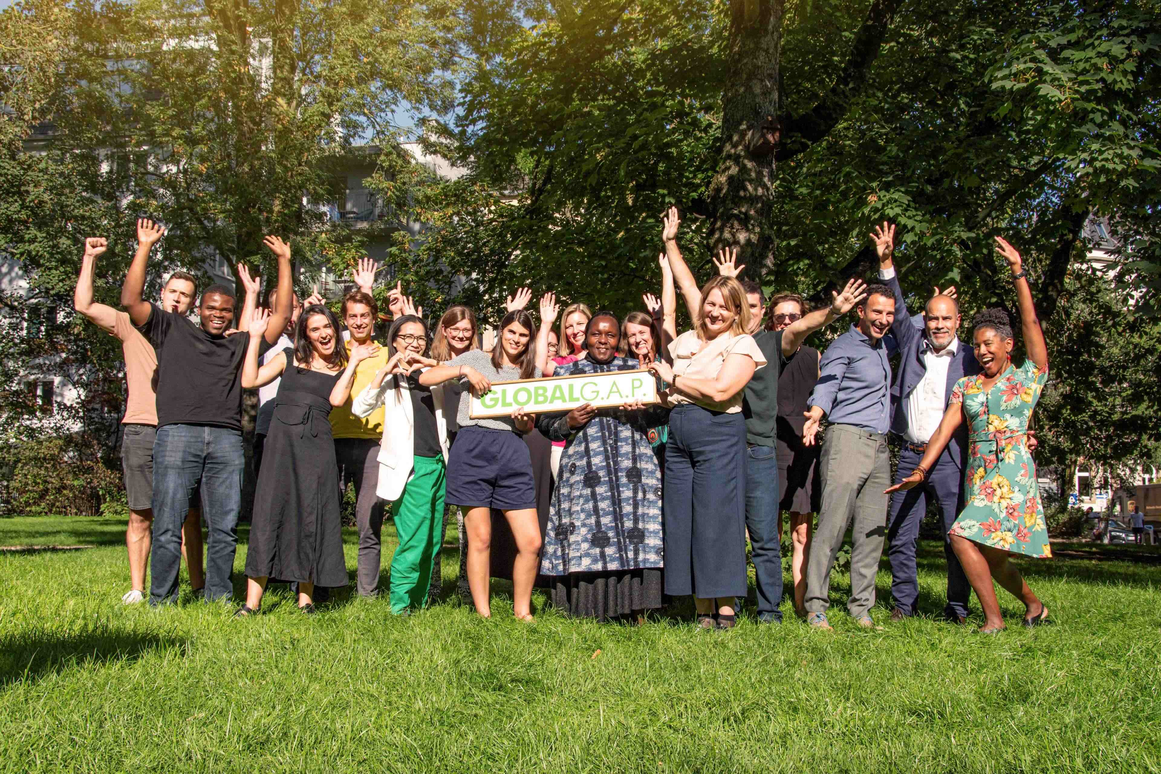Happy GLOBALG.A.P. team members holding a sign in nature